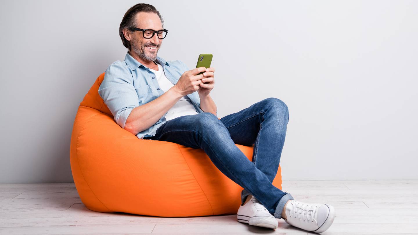 Un homme souriant consulte son smartphone assis sur un pouf