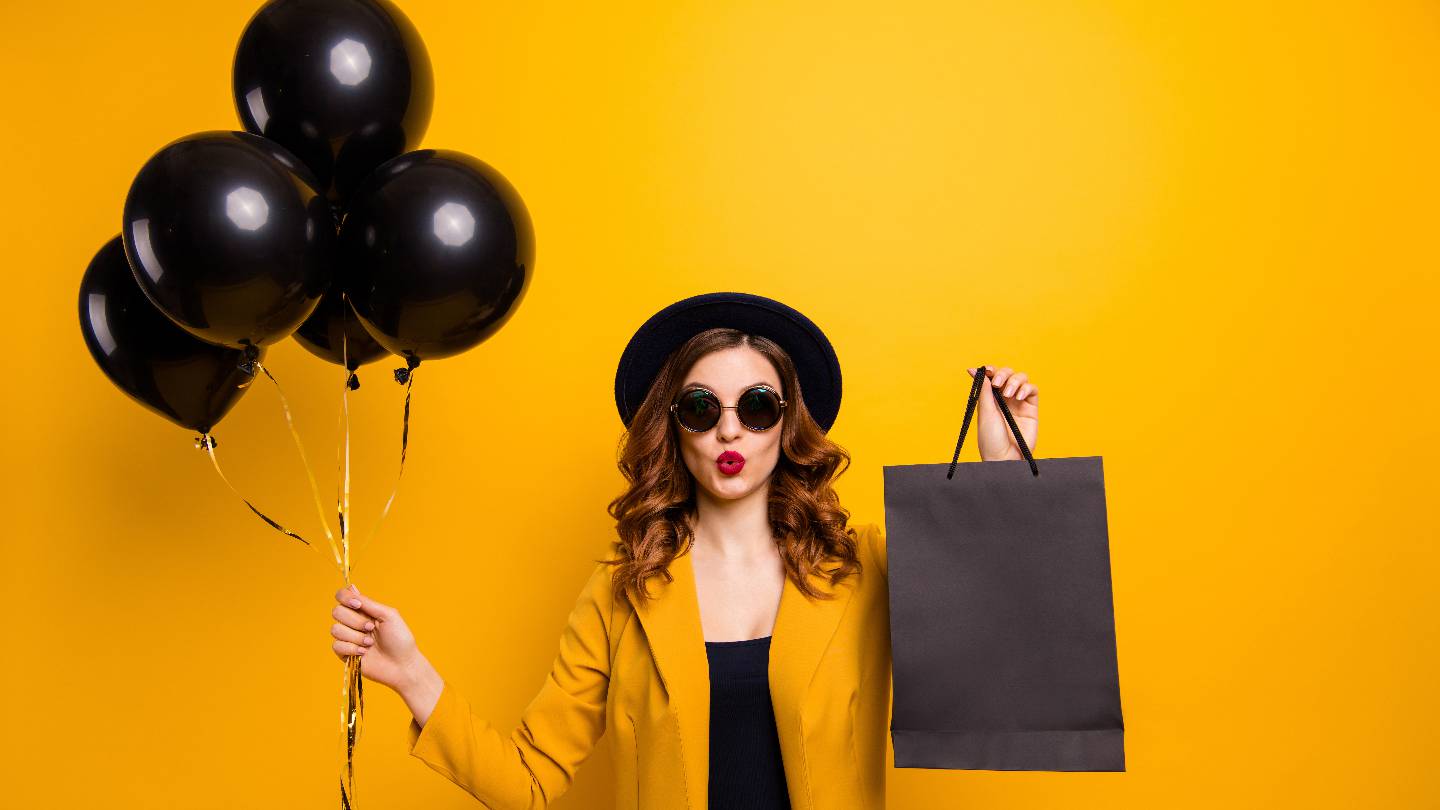 Une femme tient un sac de shopping et des ballons noirs
