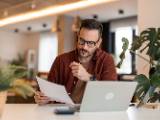 Un homme regarde son ordinateur et des documents.